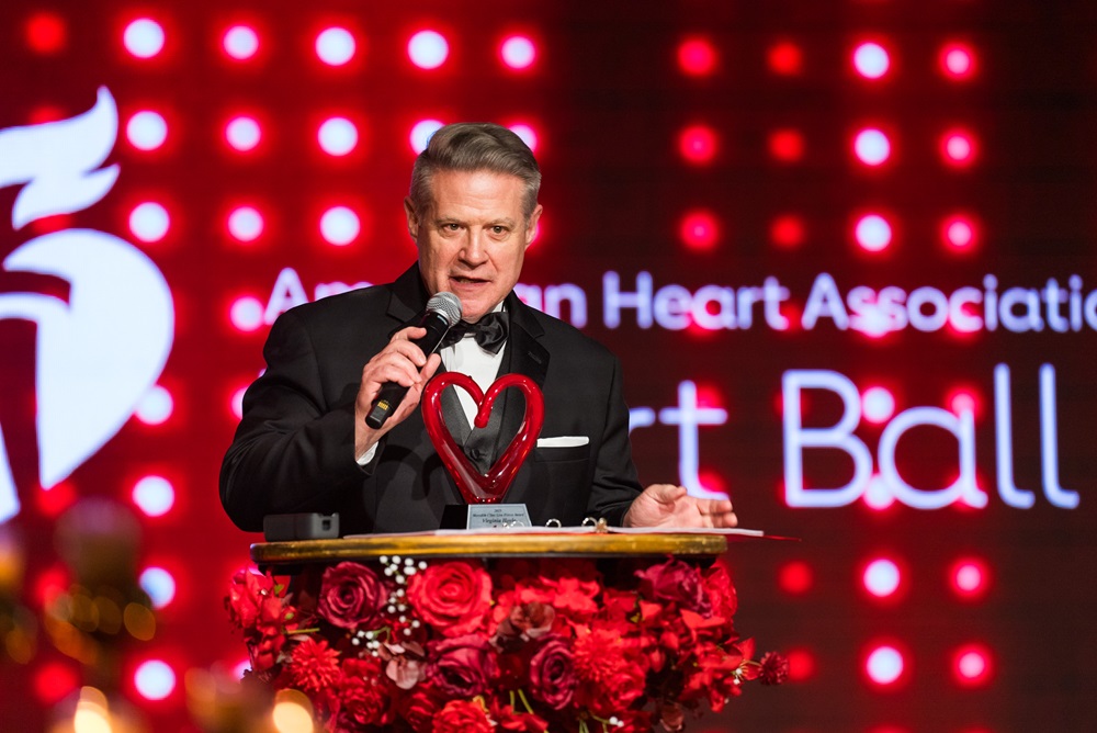 Man in tux presenting award from the podium with the American Heart Association Heart Ball logo in the background.